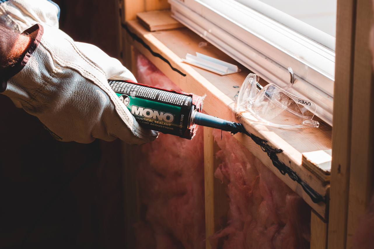 Crop worker applying sealant on seam of window in house